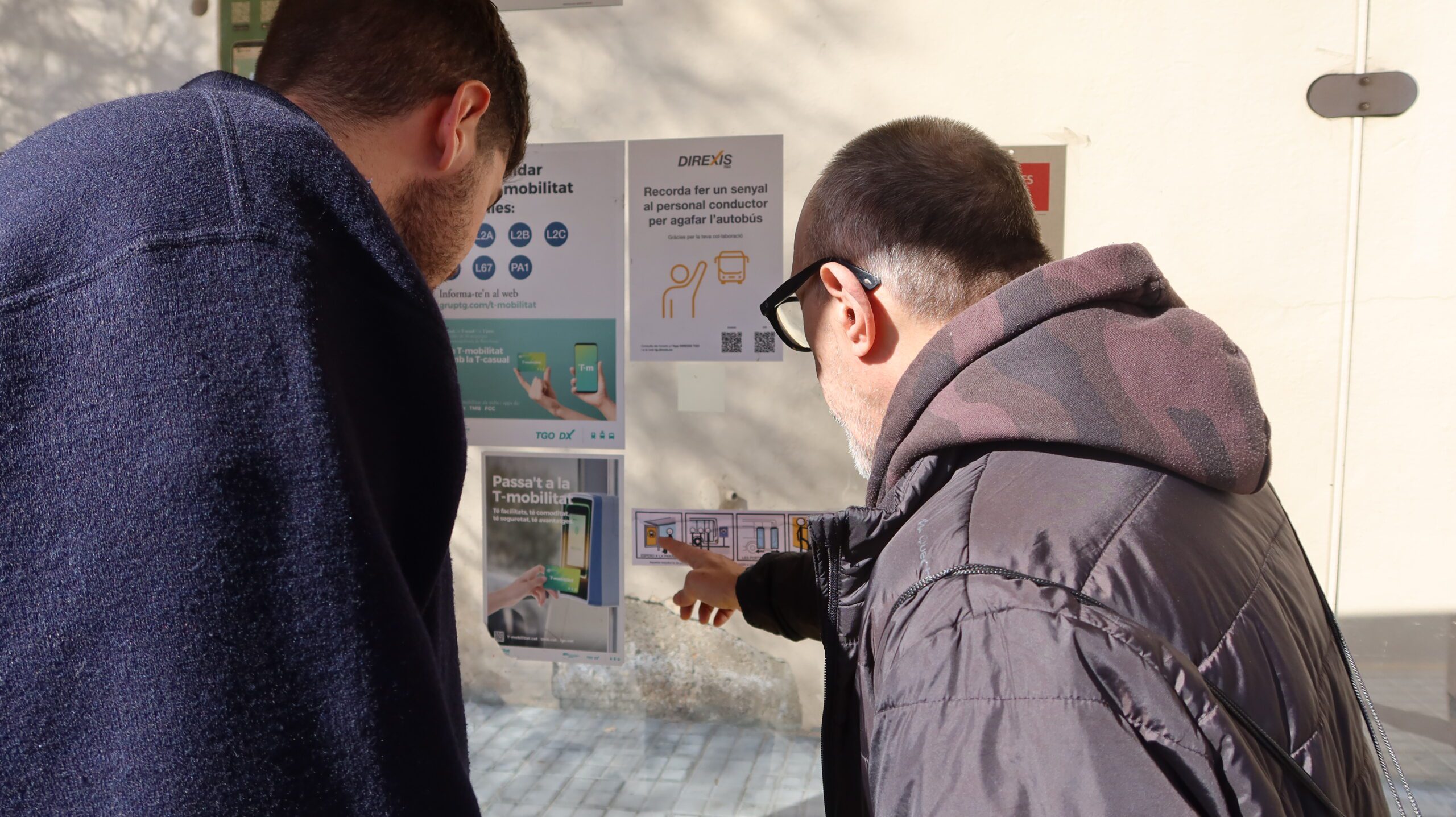 personas mirando un pictograma en una parada de autobús